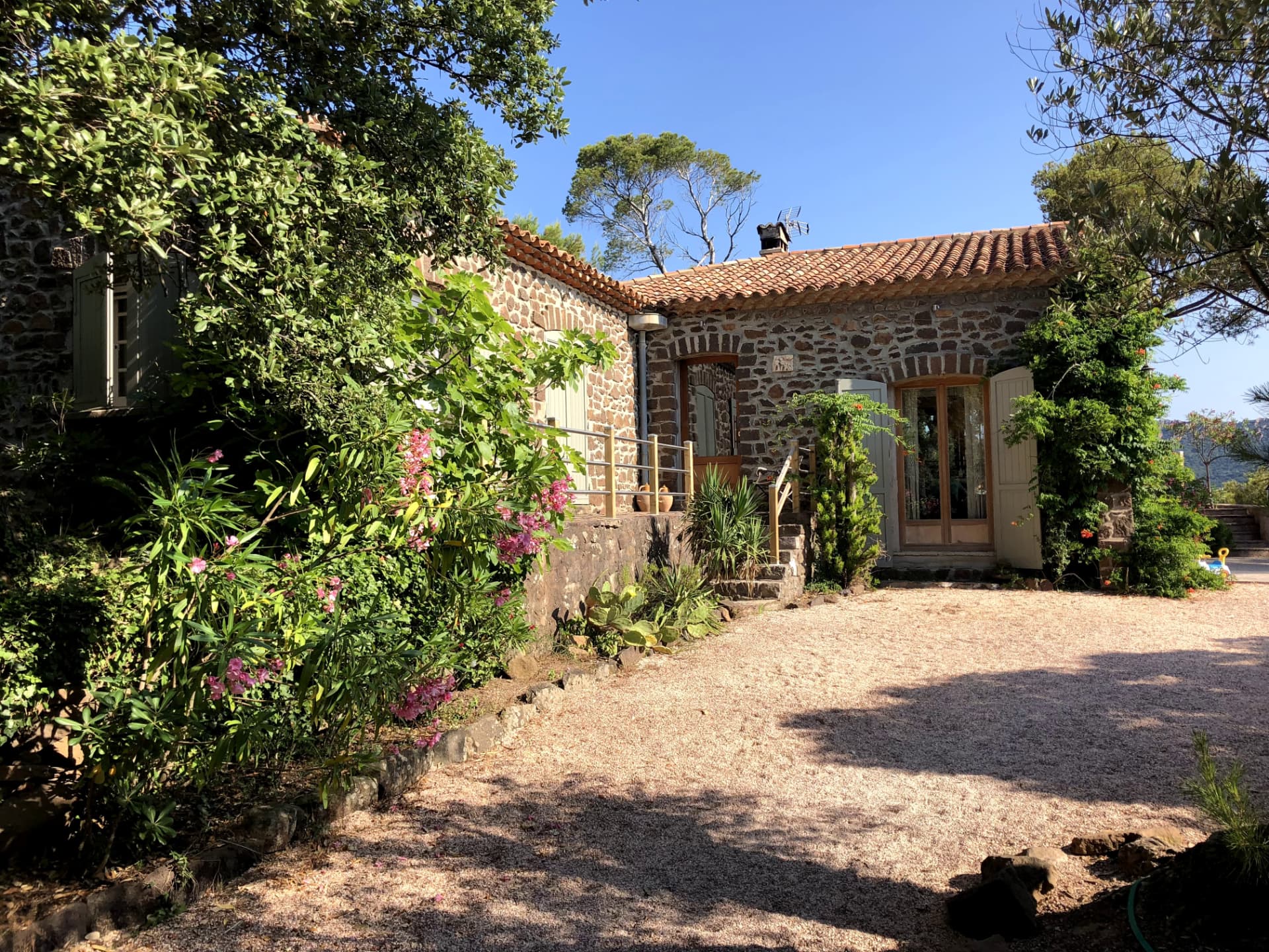 Façade en pierre de la villa, volets vert sauge et jardin fleuri de lauriers-roses