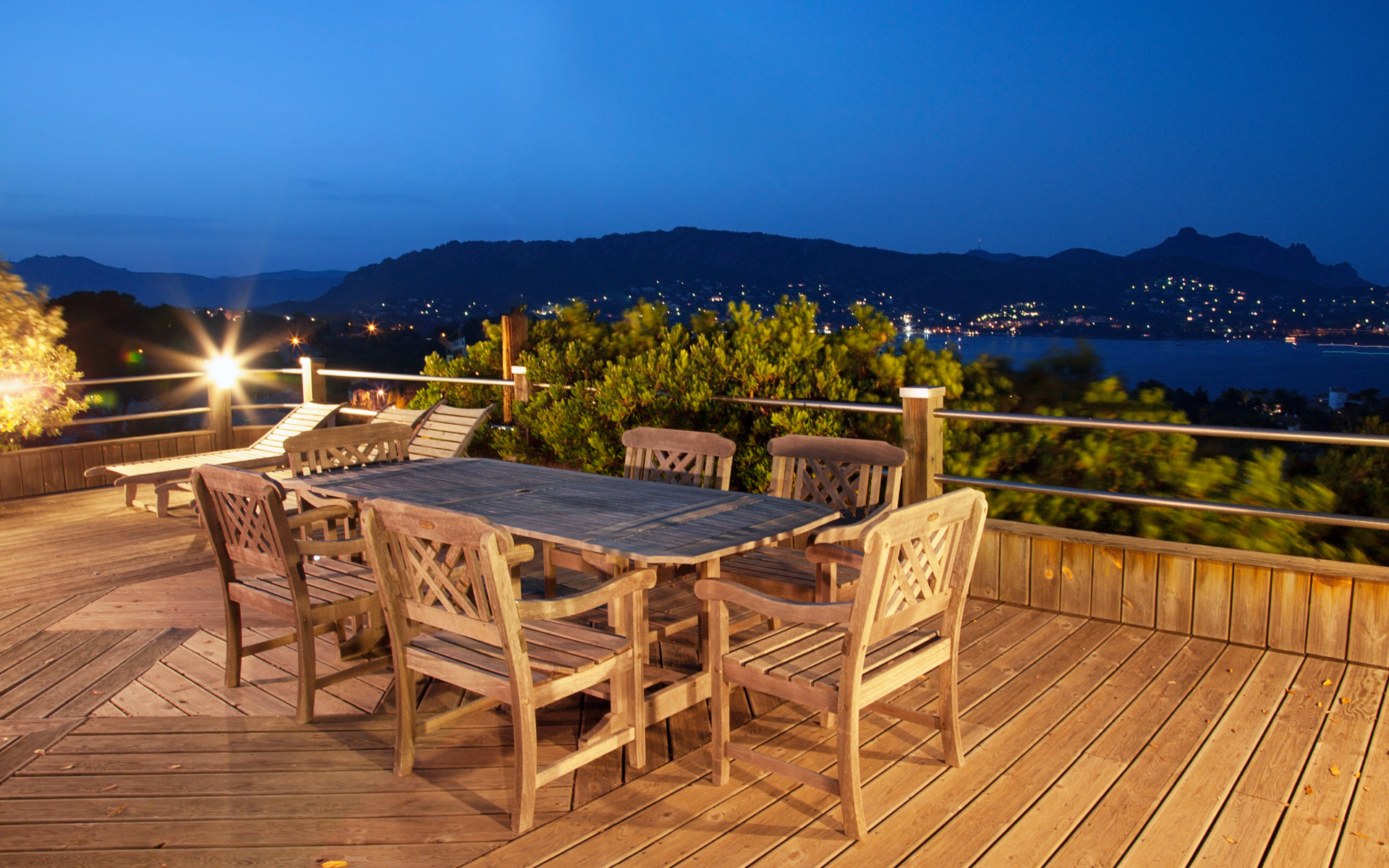 Table et transats en teck sur la terrasse au crépuscule, vue sur la baie